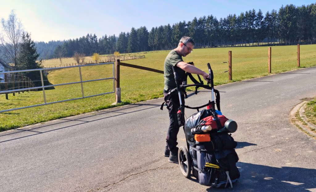 Frank packt den Wanderwagen auf einer sonnigen Straße
